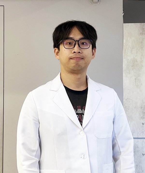 元健助聽器台北內湖店專業服務人員形象照,戴黑框眼鏡、身穿白袍的年輕男性站在門市灰色牆面前。