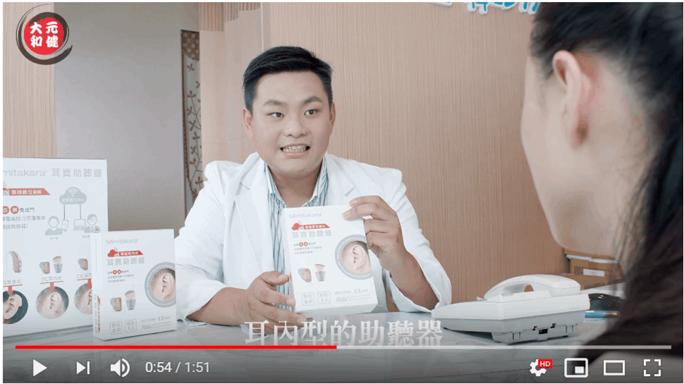 元健助聽器教學影片截圖：身穿白袍的聽力師手持助聽器包裝盒向顧客解說，桌上陳列多款助聽器盒，字幕寫著「耳內型的助聽器」，點擊閱讀〈如何更換助聽器電池？換電池不困難！元健助聽器2分鐘教學讓您看懂助聽器電池更新方式！〉