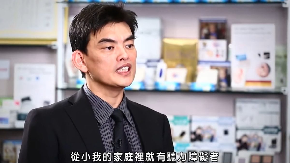 元健大和吳志賢總經理身穿黑色西裝在擺滿助聽器包裝的展示櫃前受訪,字幕寫著「從小我的家庭裡就有聽力障礙者」,點擊觀看〈「元健大和」 吳志賢總經理 研發助聽器的肇因及理念〉